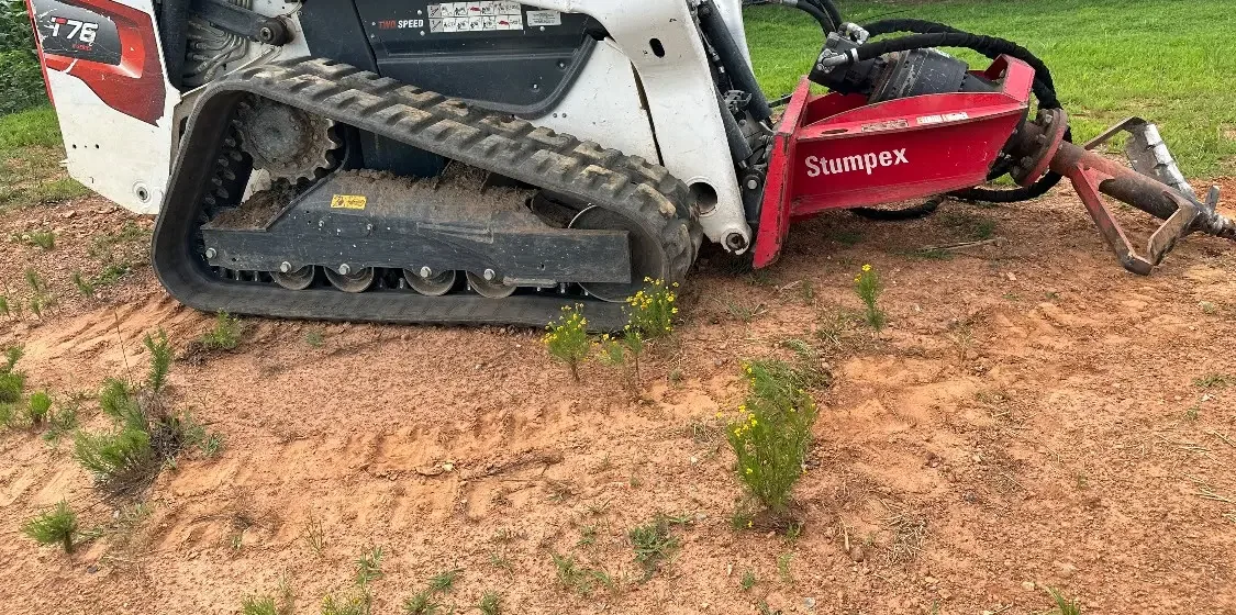 Tracked skid steer with a stump grinder attachment working a cut stump on a job near Shelby, NC